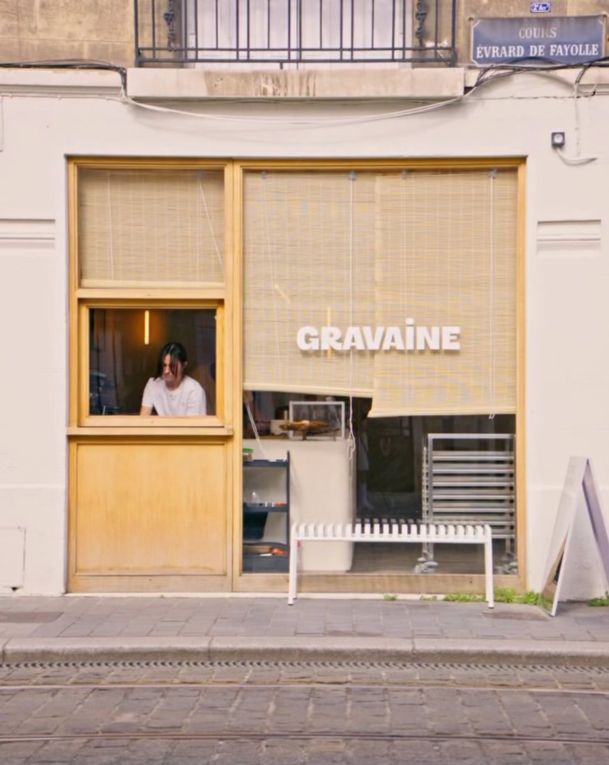 La façade de Gravaine, cours Evrard de Fayolle : vitrine encadrée de bois clair, store en bambou et enseigne GRAVAÏNE