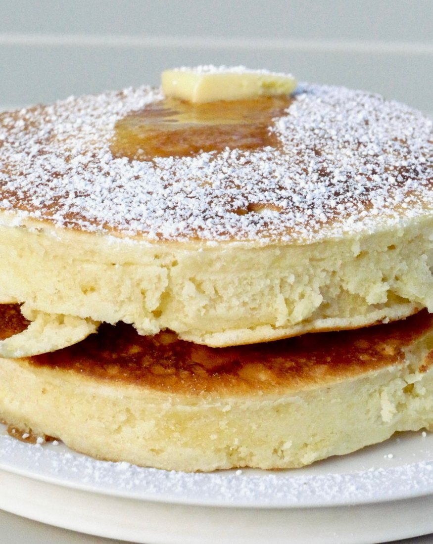 Pancakes épais saupoudrés de sucre glace, sirop et beurre